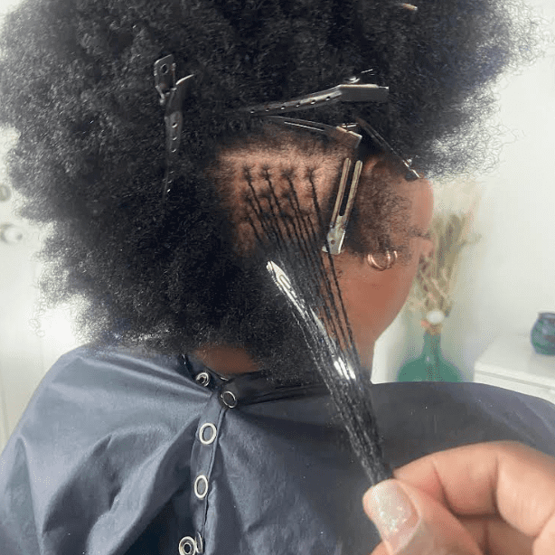 A hairstylist shaping a curly afro with scissors.